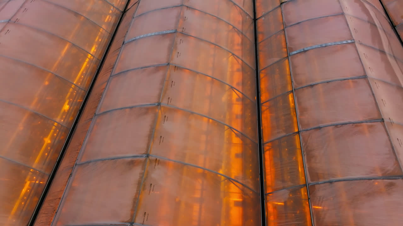 Aerial tracking shot low over the roof of a illuminated greenhouse, gloomy evening