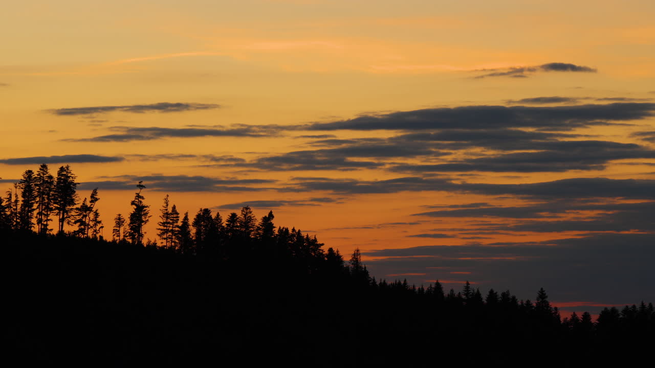 Side movement the hilltops where dark trees are hidden in the background of shadows and silhouettes of clouds moving on the horizon during sunset