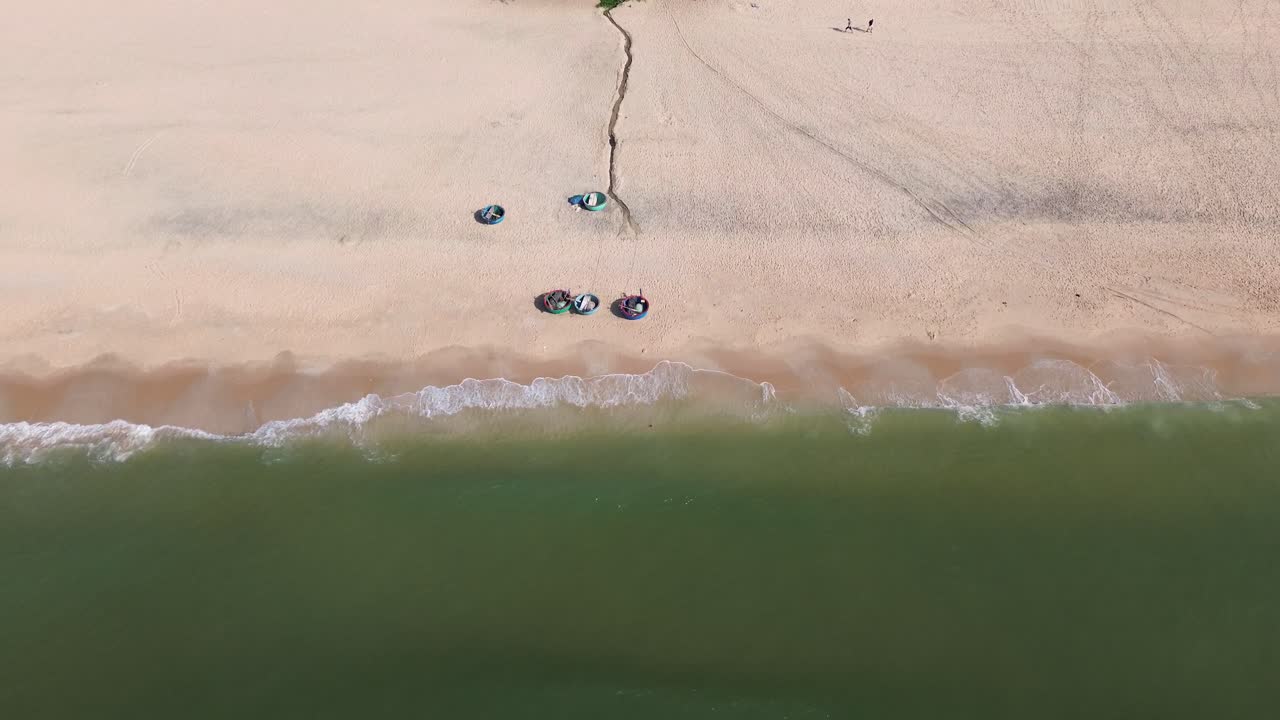 Drone flies backward facing the beach in Mui Ne, showing rows of colorful swimming buckets parked on pristine white sand with the turquoise sea in the background.