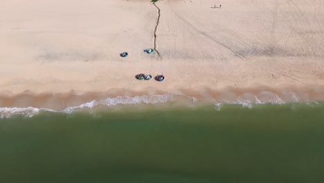 drone flies backward facing the beach in mui ne, showing rows of colorful swimming buckets parked on pristine white sand with the turquoise sea in the background.