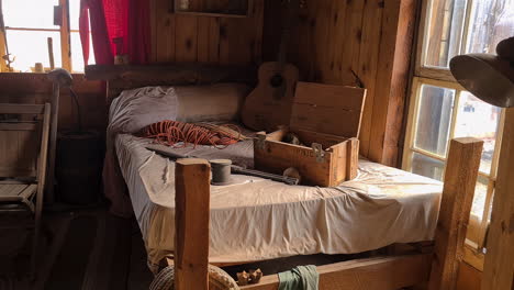 Inside-of-Old-Wooden-House-From-American-West,-Bed,-Guitar-and-Chair,-Close-Up