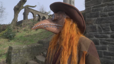 pelirroja con máscara de plaga y sombrero de vaquero de pie entre las ruinas de piedra