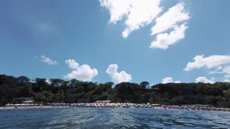 Handaufnahme-Des-Wunderschönen-Berühmten-Touristenziels-Madeiro-Strand-In-Pipa,-Brasilien-In-Rio-Grande-Do-Norte-Mit-Viel-Grünem-Laub,-Bunten-Sonnenschirmen-Und-Tropischem,-Tiefblauem-Wasser
