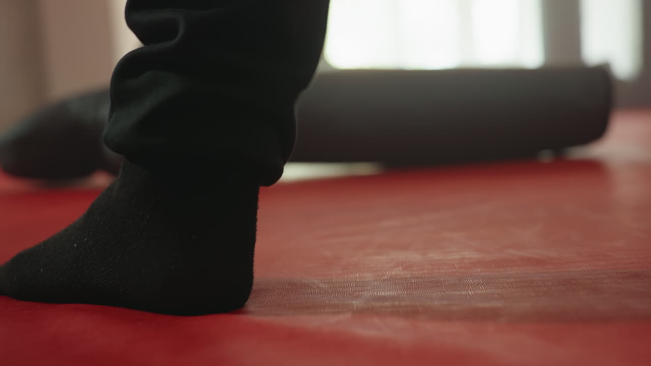 Boxer wearing black socks stands firmly on red training mat in gym, close-up of foot emphasizing stance, stability, and preparation during combat practice session,training gear visible in background