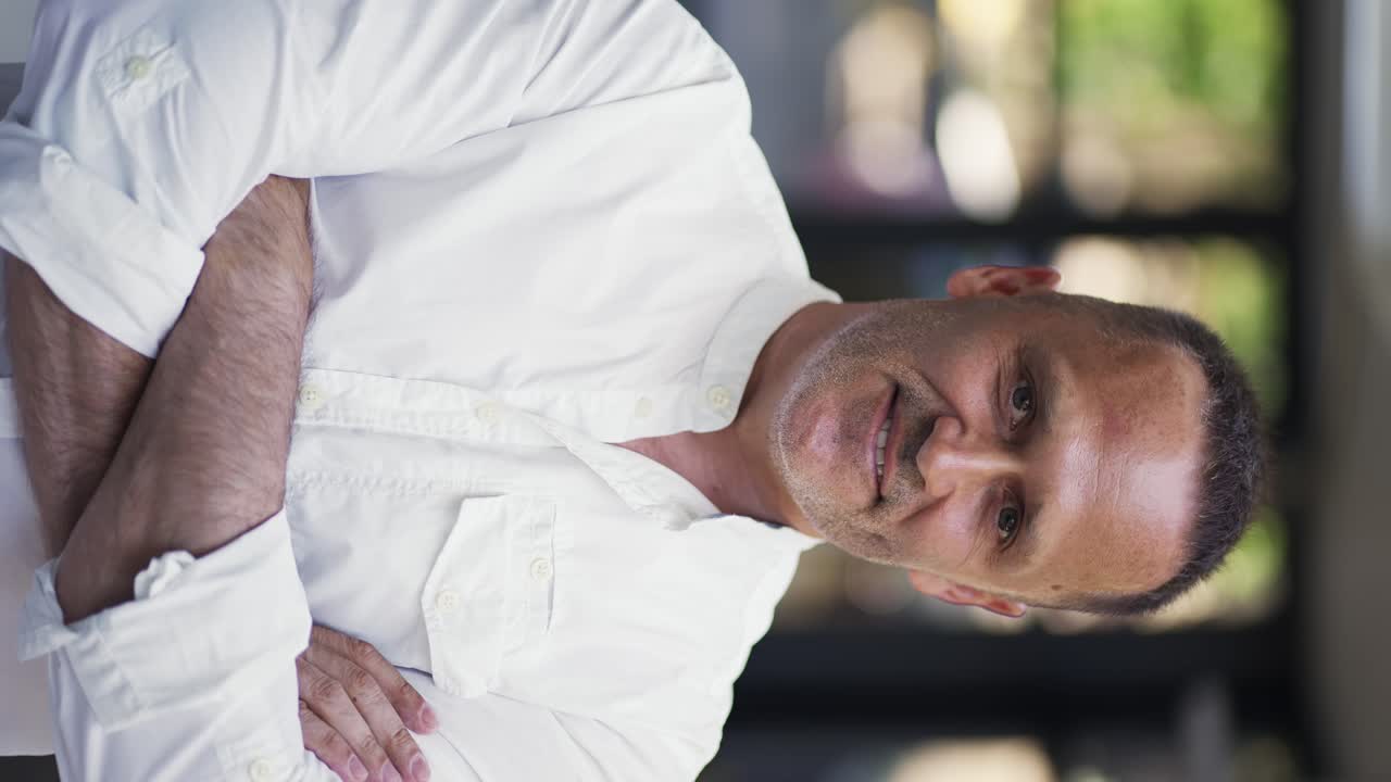and adult man with stubble in a white shirt stands in a cafe smiling and posing for the camera