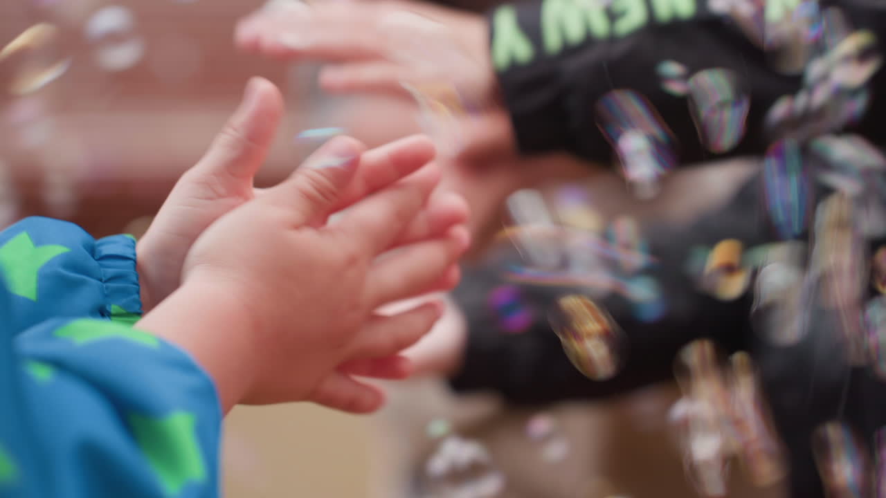 Close up of toddler hands reaching toward colorful soap bubbles in soft blur, playful outdoor moment showing curiosity, touch, and fine motor practice while children enjoy joyful sensory play