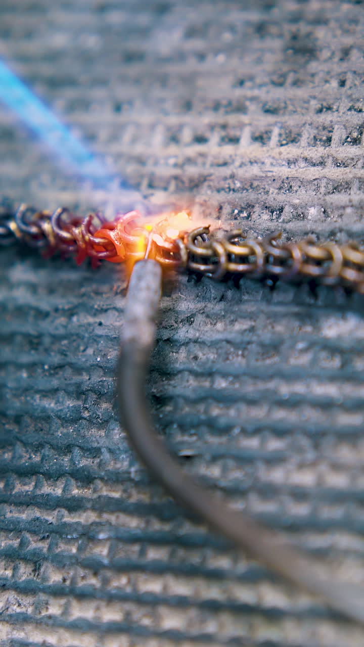 CU: processing of decorative gold metal chain part with jeweler tool and gas burner on fireproof asbestos sheet closeup