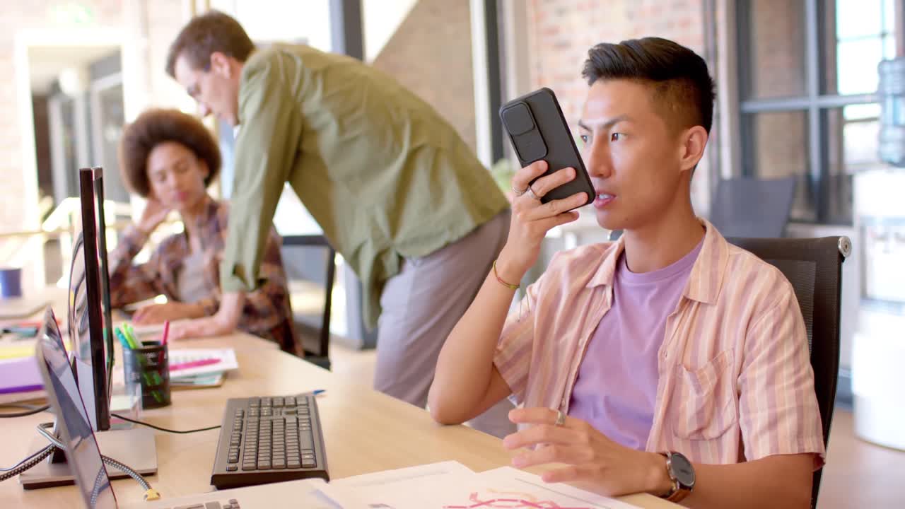 행복한 아시아 남자가 사무실에서 스마트폰으로 이야기하고, 느린 움직임을 보입니다.