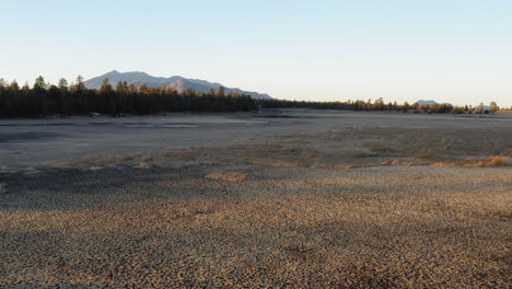 Aerial-low-angle-flight-over-parched-Lake-in-Coconino-National-Forest-and-mountain-peak-in-backdrop