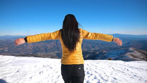 a joyful moment amidst majestic mountain landscapes: embracing nature with outstretched arms and a bright yellow jacket against a clear blue sky