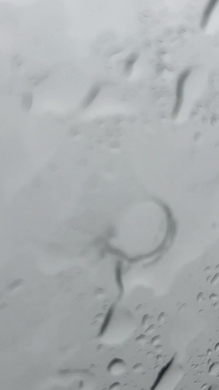 Primer plano de gotas de agua deslizándose por un cristal de ventana durante un día lluvioso. Toma vertical cinematográfica para redes sociales móviles, bienestar y conceptos de fondos evocadores.