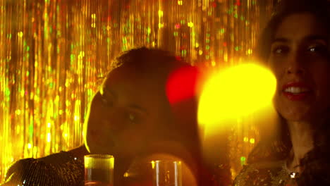 close up of two women in nightclub or bar celebrating drinking alcohol with sparkling lights 8