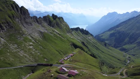 A-train-on-track-in-the-middle-of-the-mountains-of-Switzerland,-driving-down-from-Brienz-Rothorn-in-the-stunning-surroundings-of-the-mountains-of-the-Alps-of-Europe-on-a-clear-blue-day---Lake-Brienz