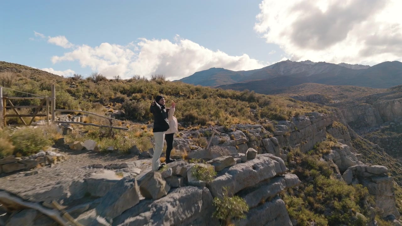 Madre e figlia stanno a braccia aperte su aspre scogliere di montagna a Tafí del Valle, Tucumán, Argentina, Valli Calchaquí e Cumbres, esprimendo libertà, legame familiare, ripresa aerea con drone in avanzamento.