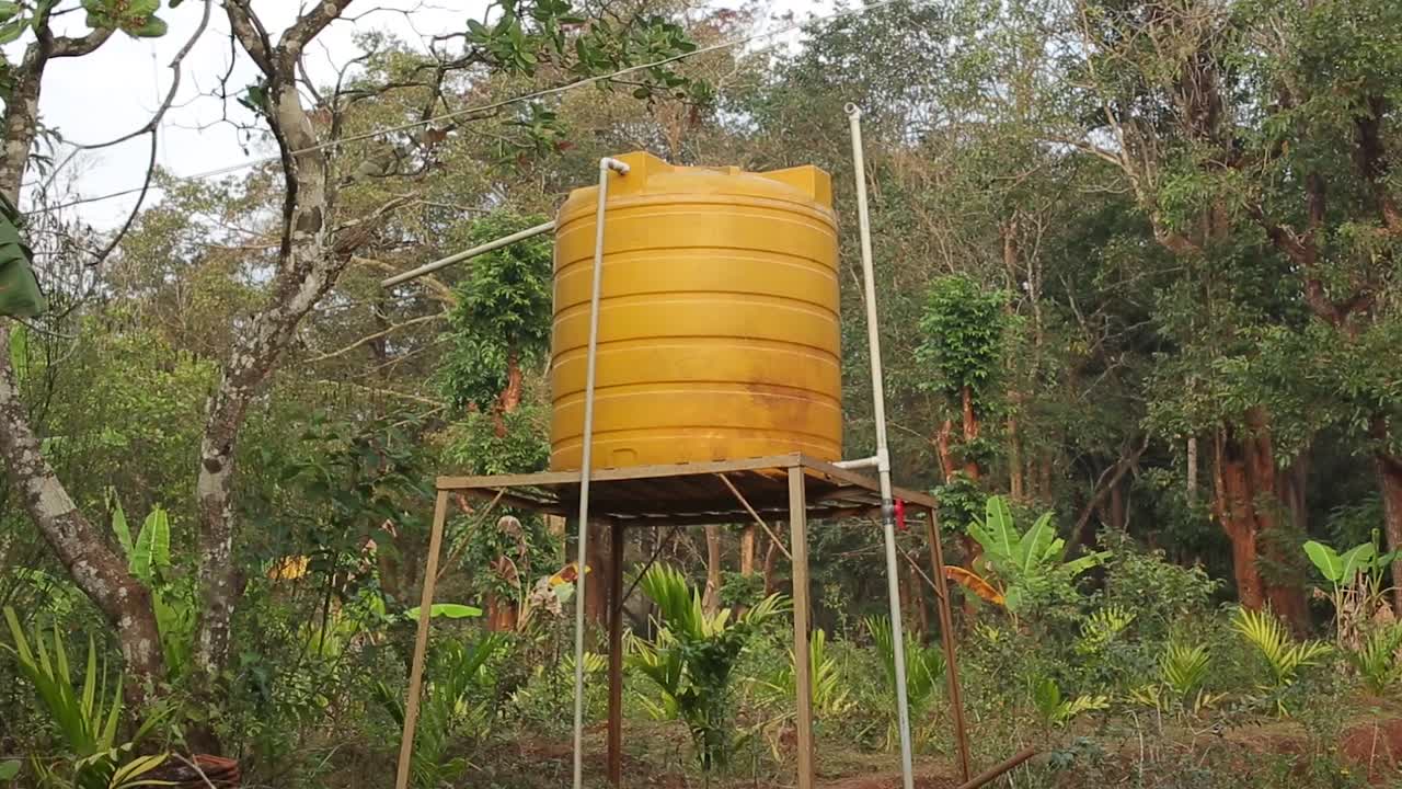 Caixa d'água amarela brilhante em torre com fundo de floresta verde