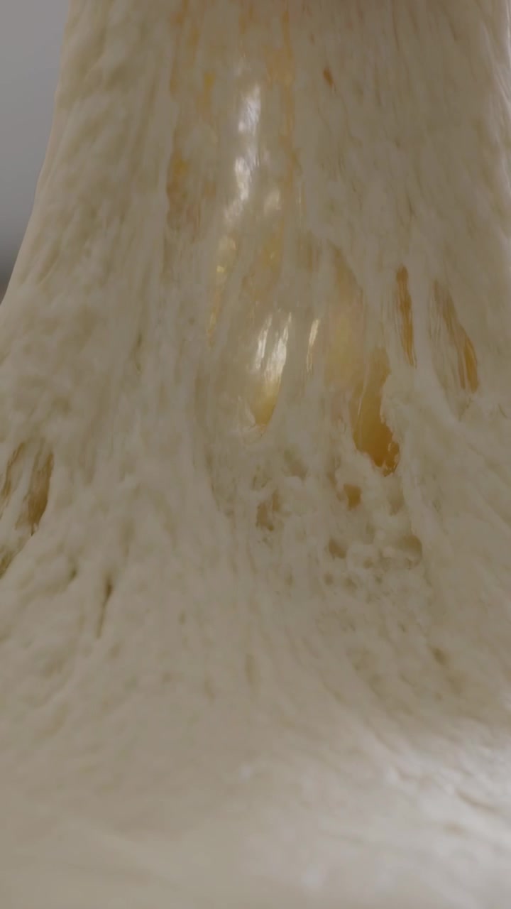 Vertical video: Pressing thumb and forefinger, hand stretching dough ball by window, testing gluten