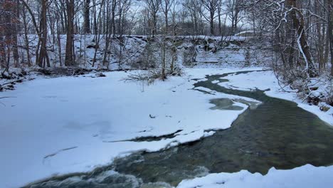 aerial drone footage of a partially frozen creek during winter in western new york state after fresh snowfall