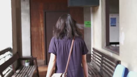 tracking rearview shot of unrecognizable woman walking through open hallway