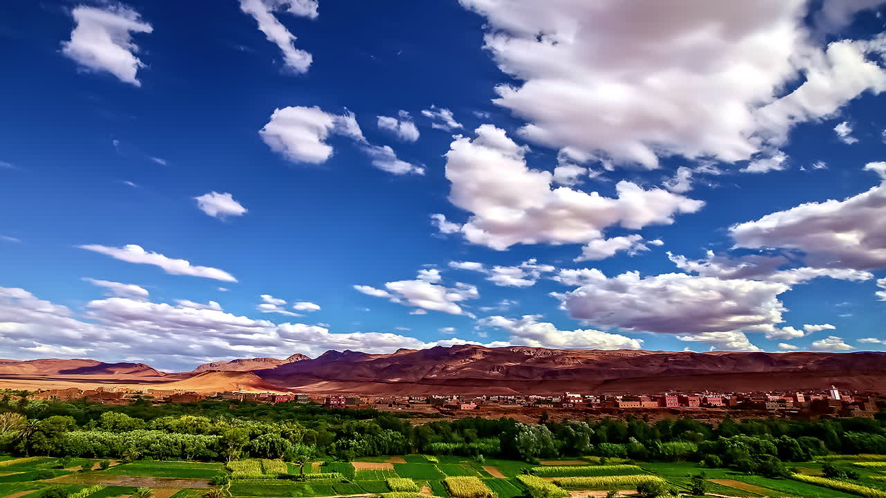 lapso de tiempo de un paisaje de tierra roja y edificios de barro junto a la vegetación verde bajo un cielo azul con nubes blancas que avanzan
