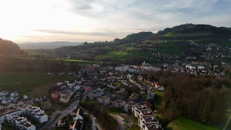 Luftaufnahme-Einer-Schweizer-Kleinstadt-Mit-Hügel-Und-Nachbarschaft-Bei-Sonnenuntergang