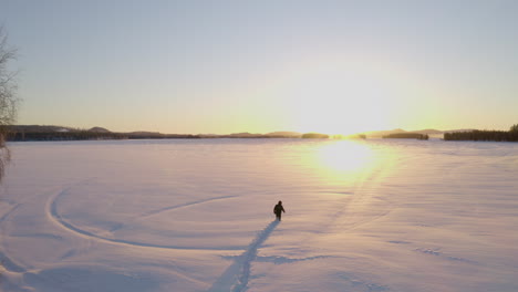 Man-walking-across-Norbotten-snow-covered-frozen-lake-on-Lapland-Polar-circle-at-sunrise