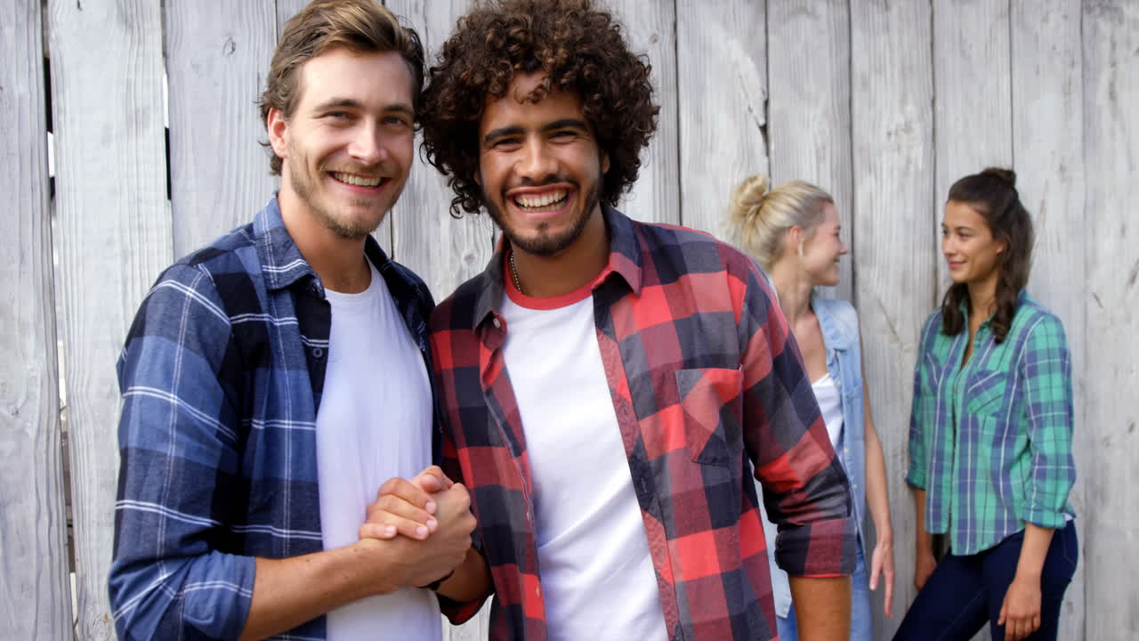 hombres jóvenes estrechando la mano mientras las mujeres interactúan en el fondo