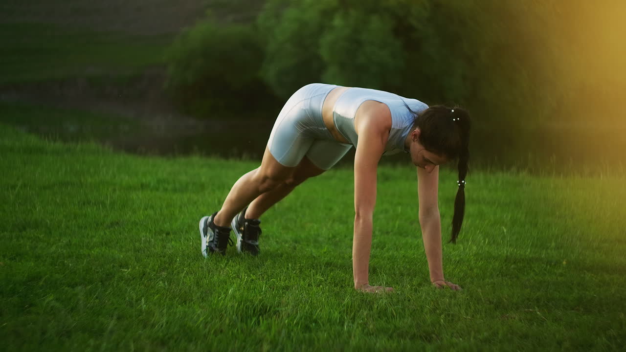 a woman in a Park on the grass stands in the plank exercise and moves her legs left and right in turn. static exercise on abs