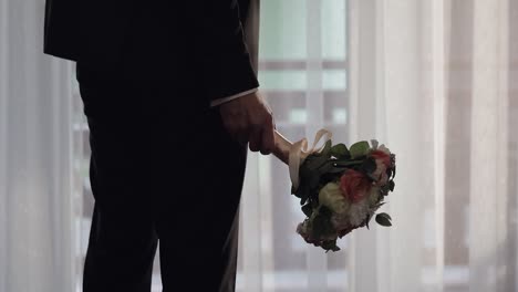 Groom-with-wedding-bouquet-in-his-hands-at-home.-White-shirt,-jacket