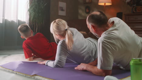 family doing sports at home together grandparents and grandson excercising at home and doing a leg muscle workout on a fitness mat together