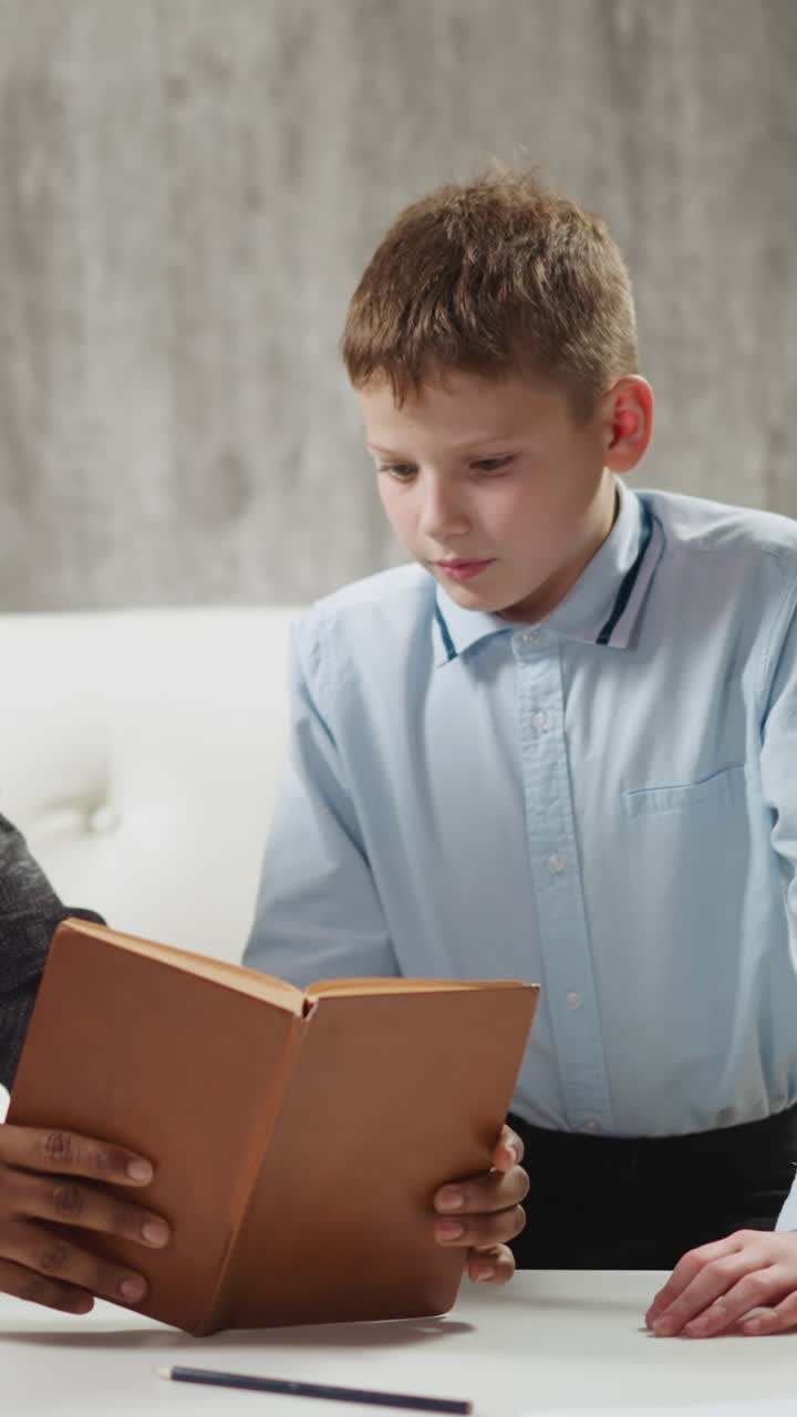 Skilled African-American teacher shows exercise in textbook to junior student at private English language tuition with native speaker slow motion