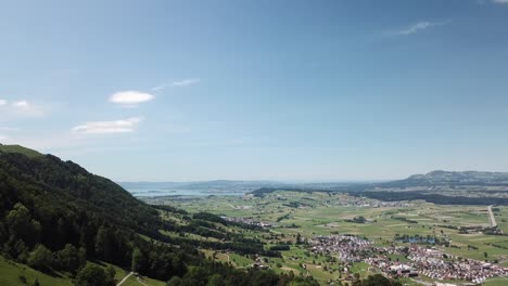 drone flies over a hill with two sheds on a small green hill next to a valley with some villages in switzerland near to the lake of walen