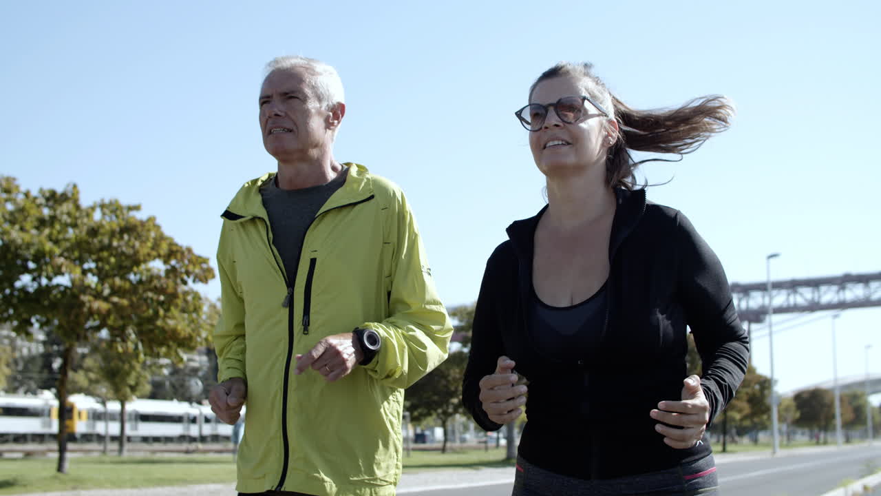 feliz pareja activa de corredores maduros trotando por la calle