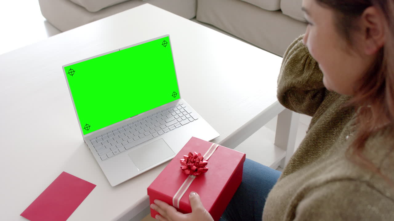 Caucasian woman holding red gift using laptop with blank space on green screen