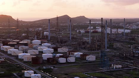 aerial orbit around oil refinery stacks and complex network pipes at sunset