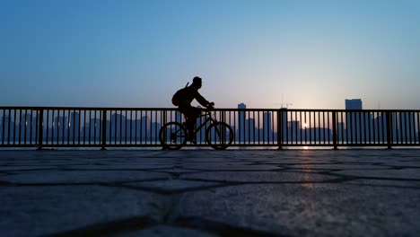 slow-motion-silhouette: a man exercising-cycling with a city skyline in the background in sharjah, united arab emirates