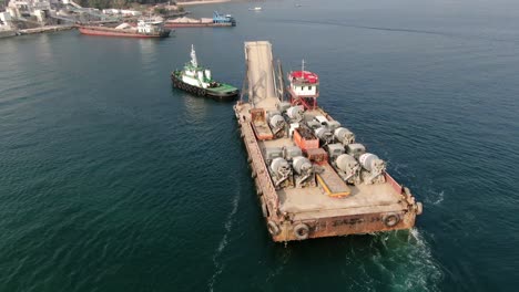 barge loaded with concrete mixer trucks pulled to port by a tugboat in hong kong bay, aerial view