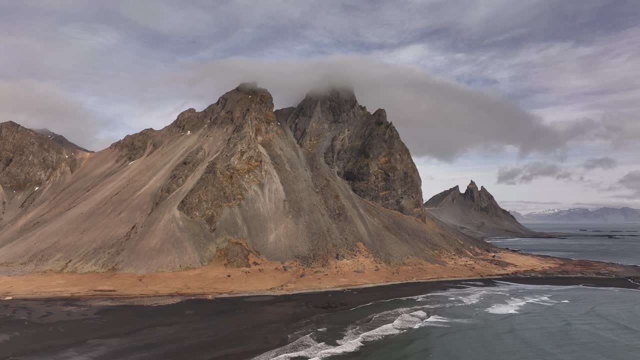 Vestrahorn and Brunnhorn rise over black beach and crashing waves on Iceland's Stokksnes peninsula. Stokksnes, Iceland