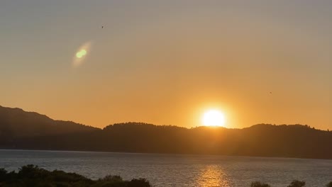 lens flare of sun through huge river on panorama of mountain landscape at sunrise and bright disk of sun in morning in summer against blue sky aerial view of drone forward