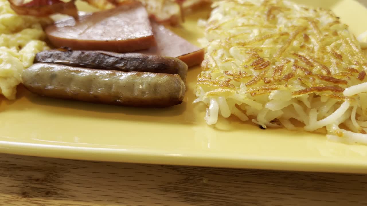 Golden hash browns with sausage and ham slices, served on a bright yellow plate