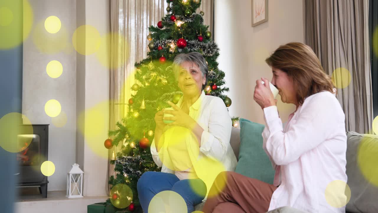 Two women with mugs talking left gesturing sparking laugh yellow bokeh passing over faces marketing