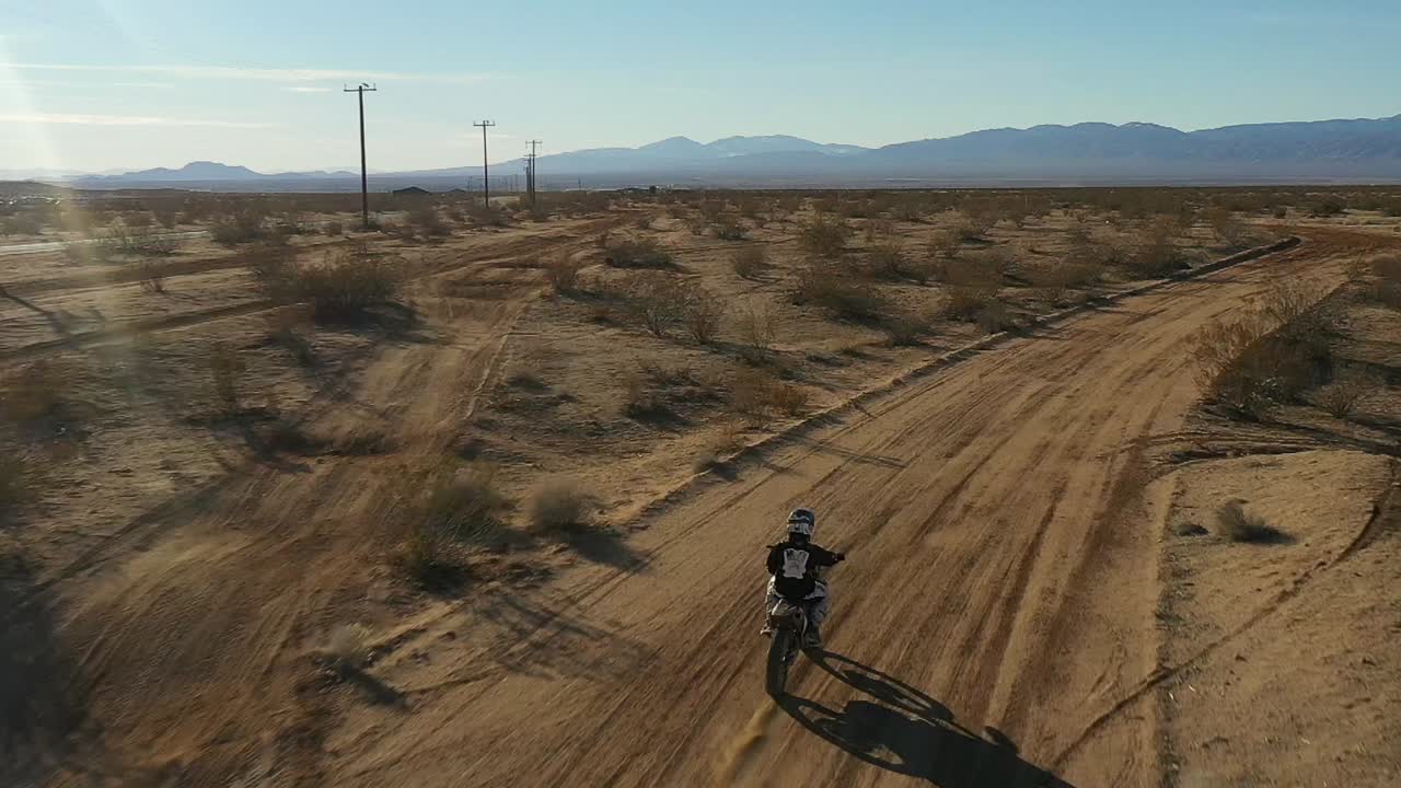 motociclista todoterreno recorriendo un camino de tierra en el desierto de mojave - vista aérea en cámara lenta
