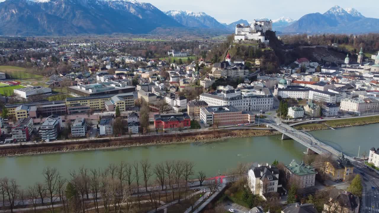Drone view overlooking Salzburg City, Salzach River, Hohensalzburg Fortress and Snow-topped Alps - Austria