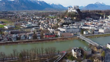 drone view overlooking salzburg city, salzach river, hohensalzburg fortress and snow-topped alps - austria