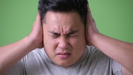 young handsome overweight asian man against green background