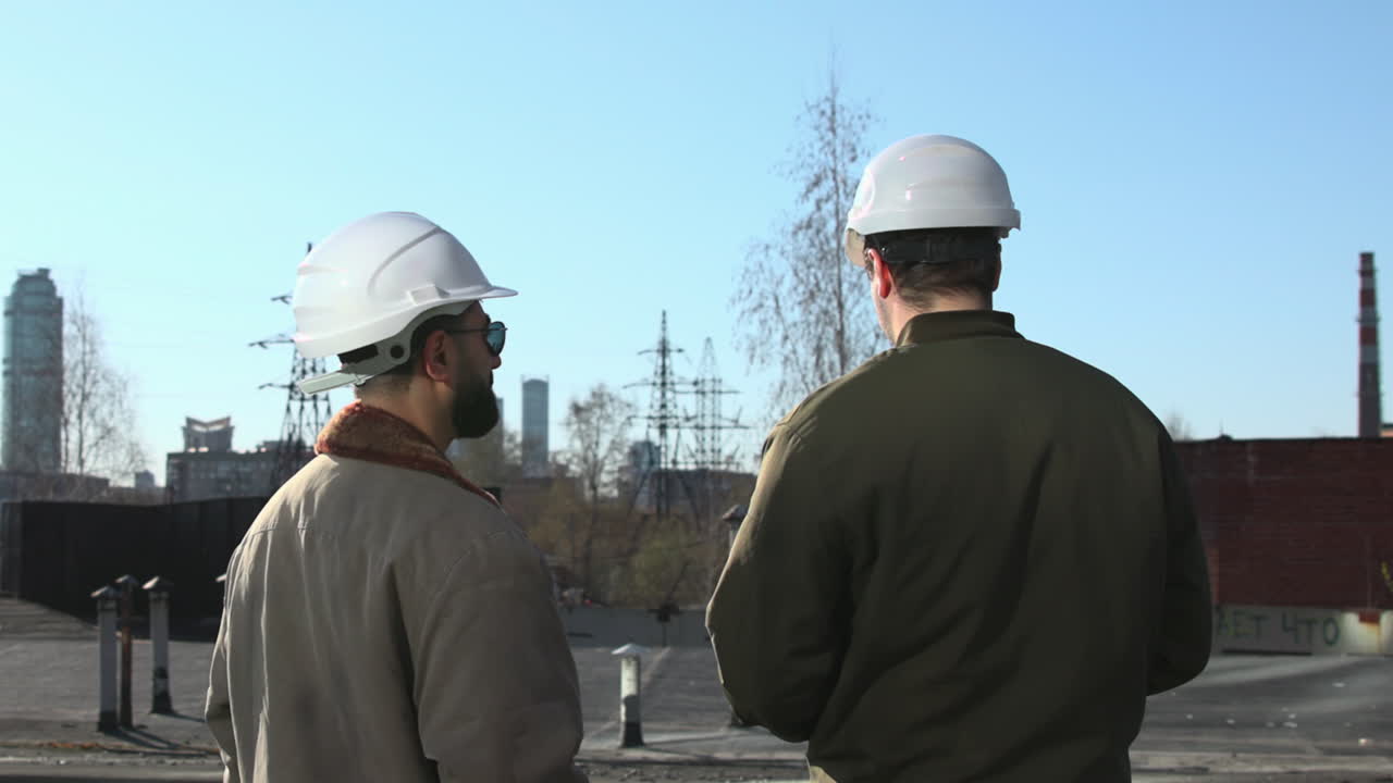 Два кавказских руководителя объекта на крыше просматривают планшет, сверяя схемы и заметки, бородатый прораб.