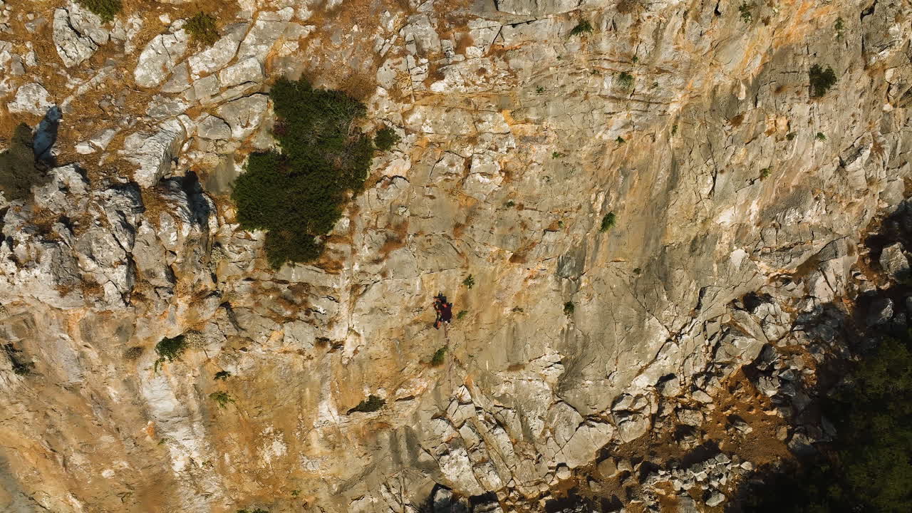 Aerial view tilting toward a person rope climbing a steep mountain wall, sunrise