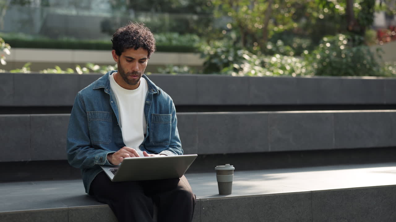 Ung mann som jobber på laptop utendørs med kaffe