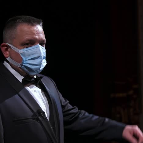 theater actor speaks on a stage in medical mask. announcer in suit stands in front of empty theater hall. pandemic concept