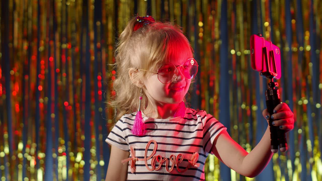 niño blogger sonriendo, grabando video blog vlog en su teléfono inteligente en un club nocturno con luz de neón roja