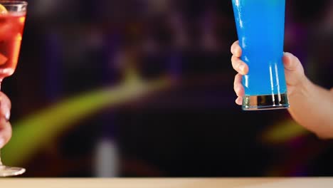 two vibrant cocktails, one red and one blue, are clinked together in a lively, colorful environment